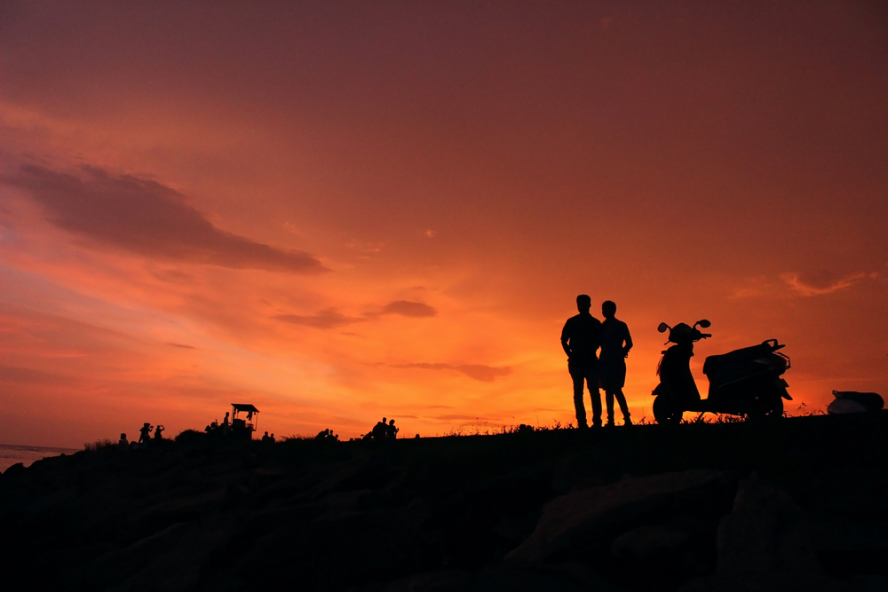 Silhouette of a couple with a scooter watching a sunset, capturing the vibe of the most romantic places in India