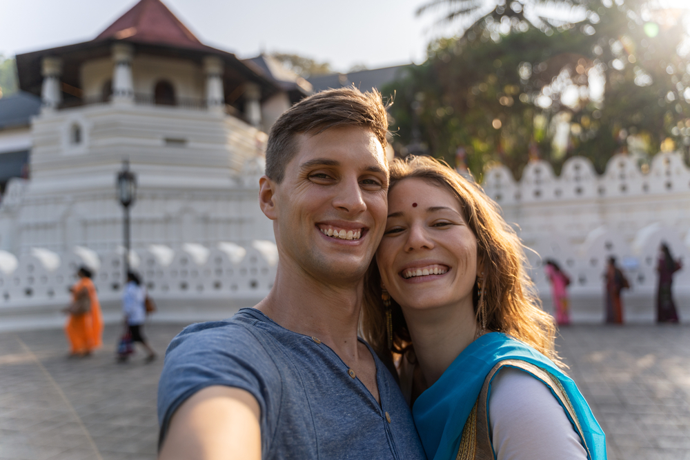 Romantic couple taking a selfie in front of the Temple of the Tooth Relic in Kandy during their srilanka honeymoon.