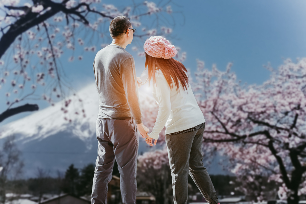 Romantic couple holding hands with Mount Fuji and cherry blossoms, a quintessential scene for a Japan honeymoon