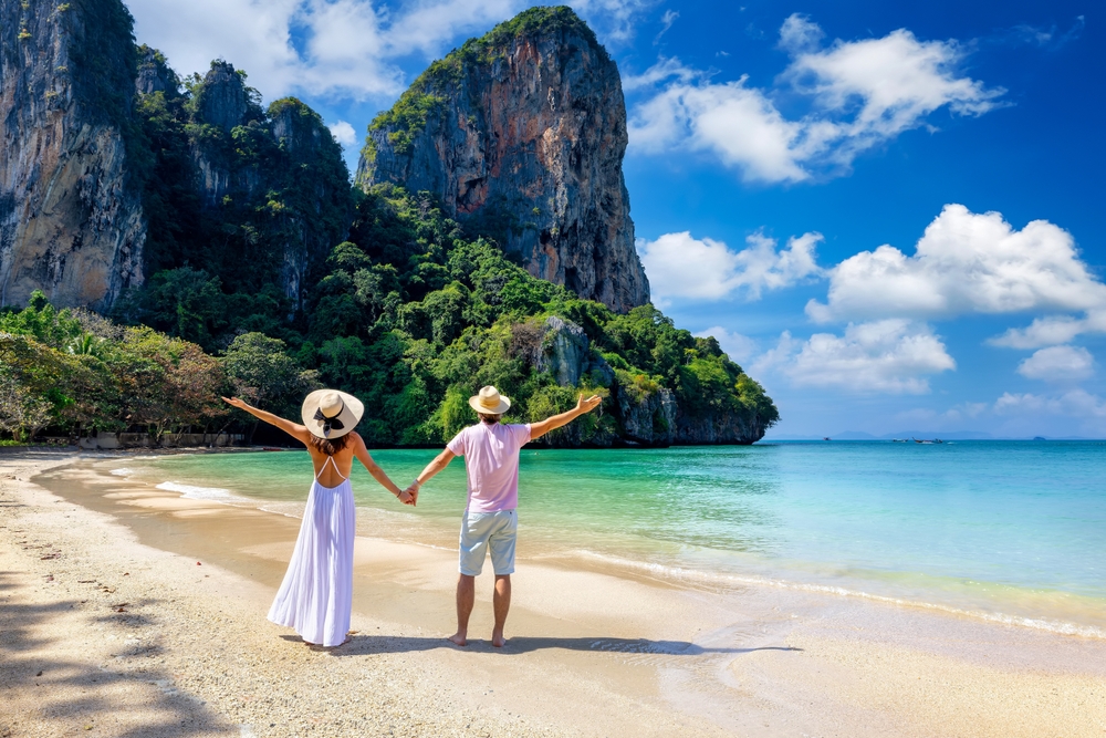Romantic couple embracing on a white sand beach facing limestone cliffs during their Krabi honeymoon in Thailand
