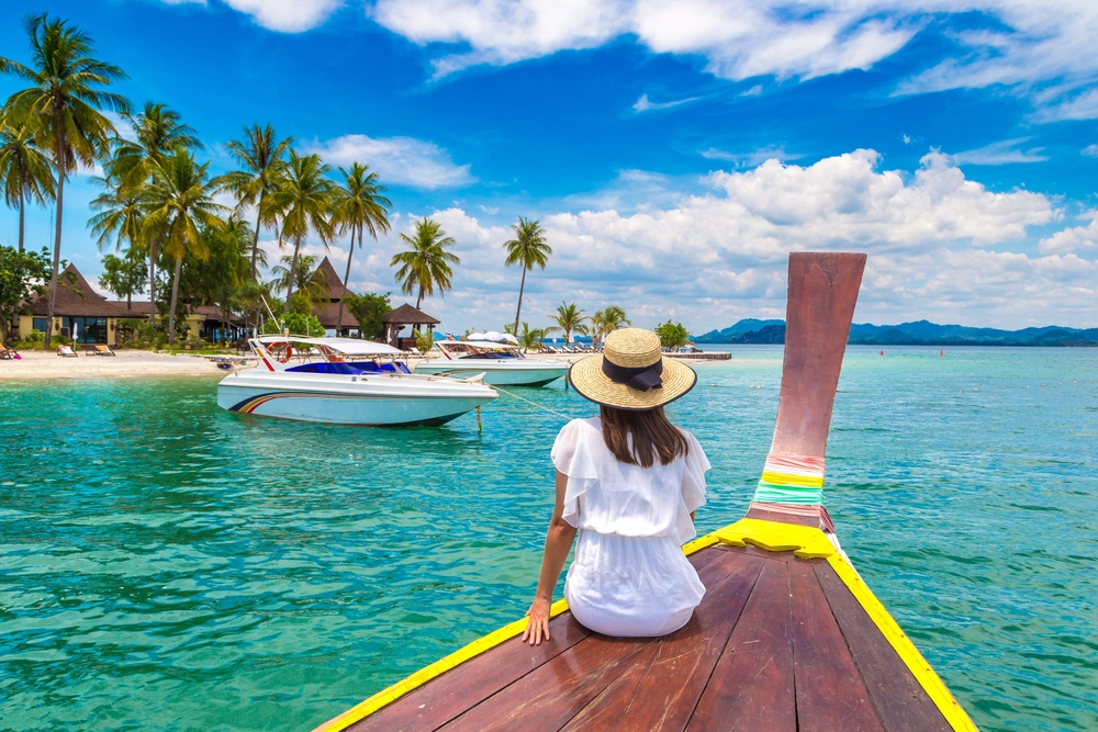 A woman on a traditional boat looking at a tropical beach during a Koh Samui honeymoon.