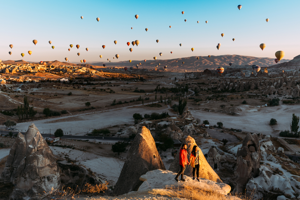 Couple standing on a rock formation in Cappadocia watching hot air balloons during their Turkey honeymoon 