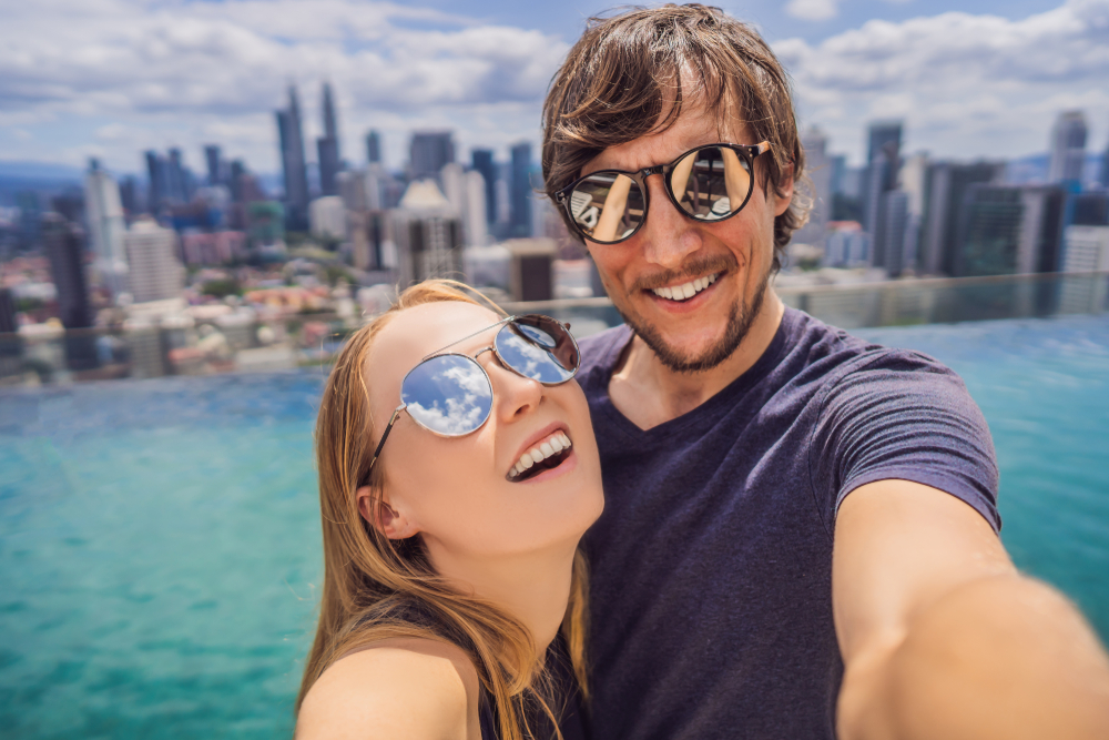 A happy couple taking a selfie in a rooftop infinity pool, enjoying one of the most romantic places in Singapore during their honeymoon