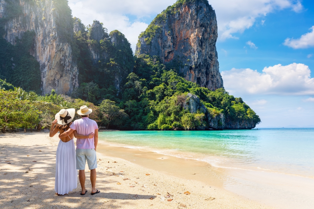 Romantic couple standing on a white sand beach facing limestone cliffs during their Krabi honeymoon in Thailand 