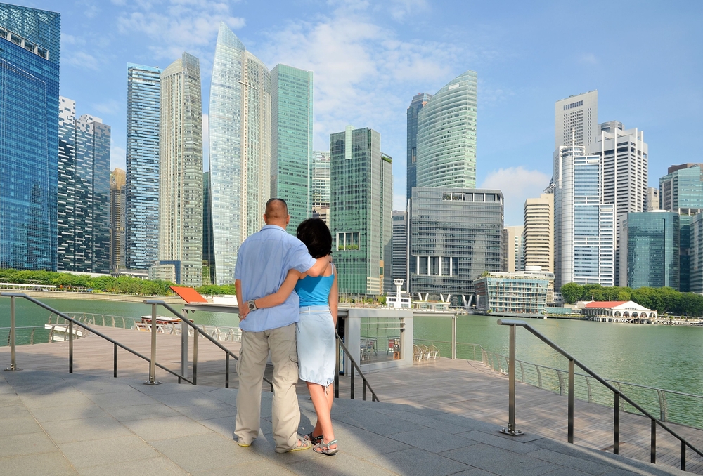 Back view of a couple embracing on a waterfront deck while admiring the skyline, representing romantic things to do in Singapore