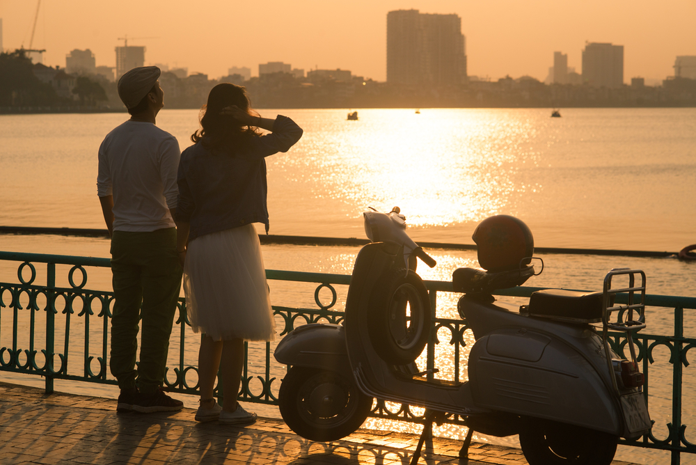 Couple watching the sunset over the lake with a scooter nearby, a romantic experience on their Hanoi Honeymoon