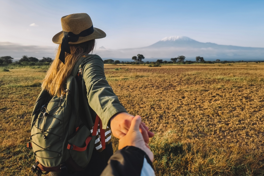 A couple holding hands while walking through a savanna toward Mount Kilimanjaro during a romantic Tanzania honeymoon.