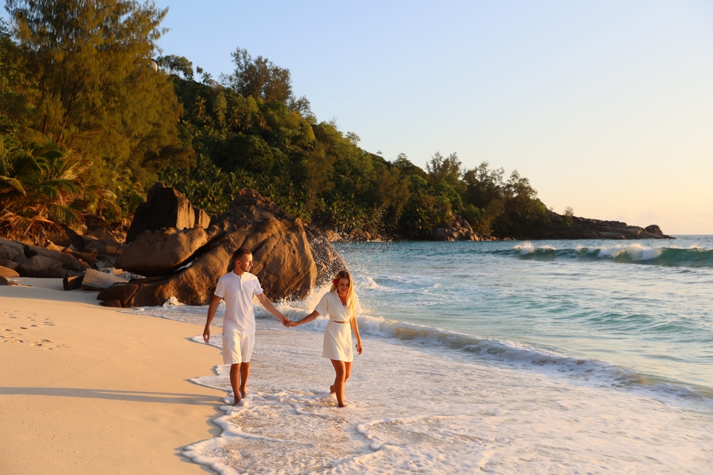 Couple walking along a white sand beach during a honeymoon Seychelles island getaway