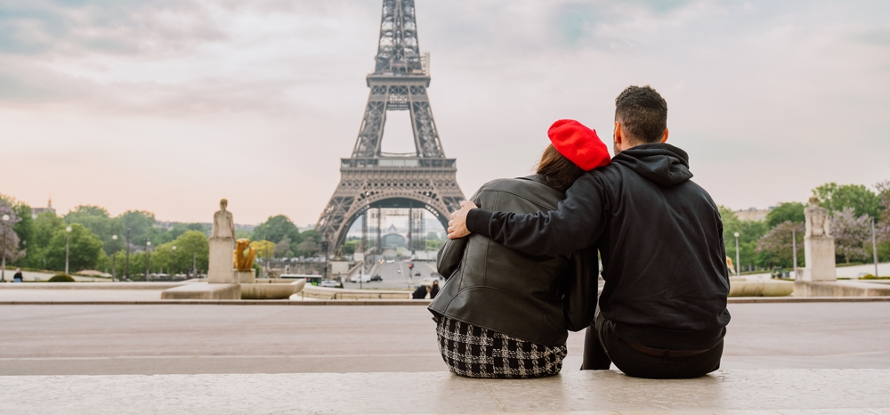 A couple sits on a wall overlooking the Eiffel Tower in Paris, a classic stop for travelers researching cheap honeymoon destinations in Europe. 