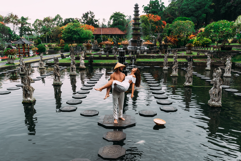 Couple on stone stepping stones at Tirta Gangga, a must-see when choosing Bali or Mauritius for a honeymoon.