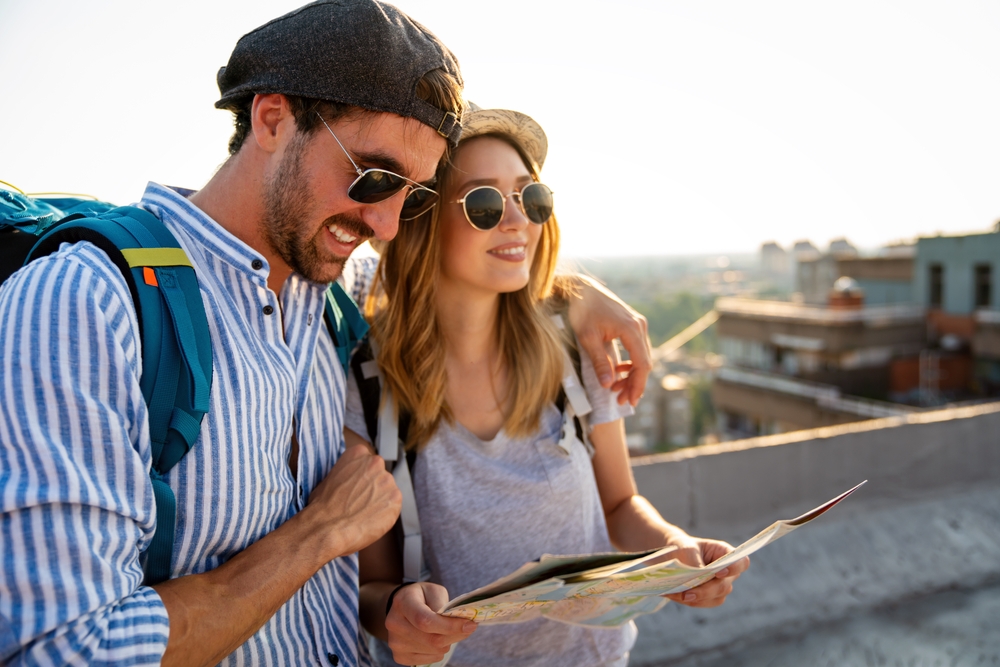 A happy couple with backpacks looking at a map on a city rooftop during their Europe honeymoon at sunset.
