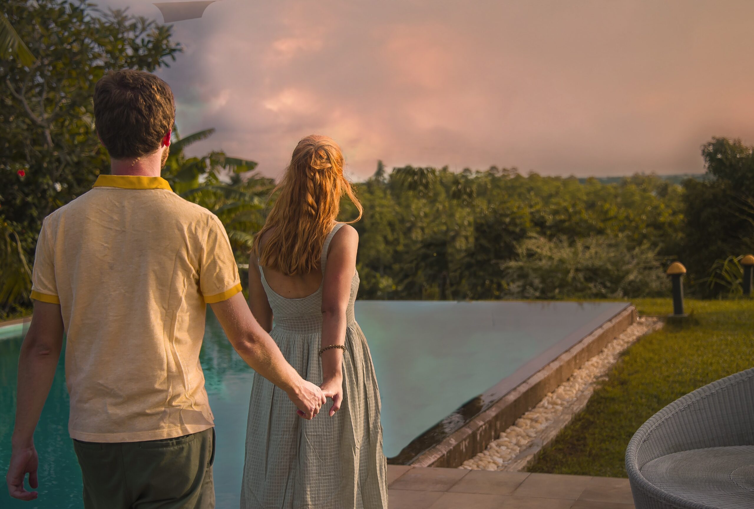 A romantic couple walking hand-in-hand toward an infinity pool at a luxury resort in Sri Lanka during sunset