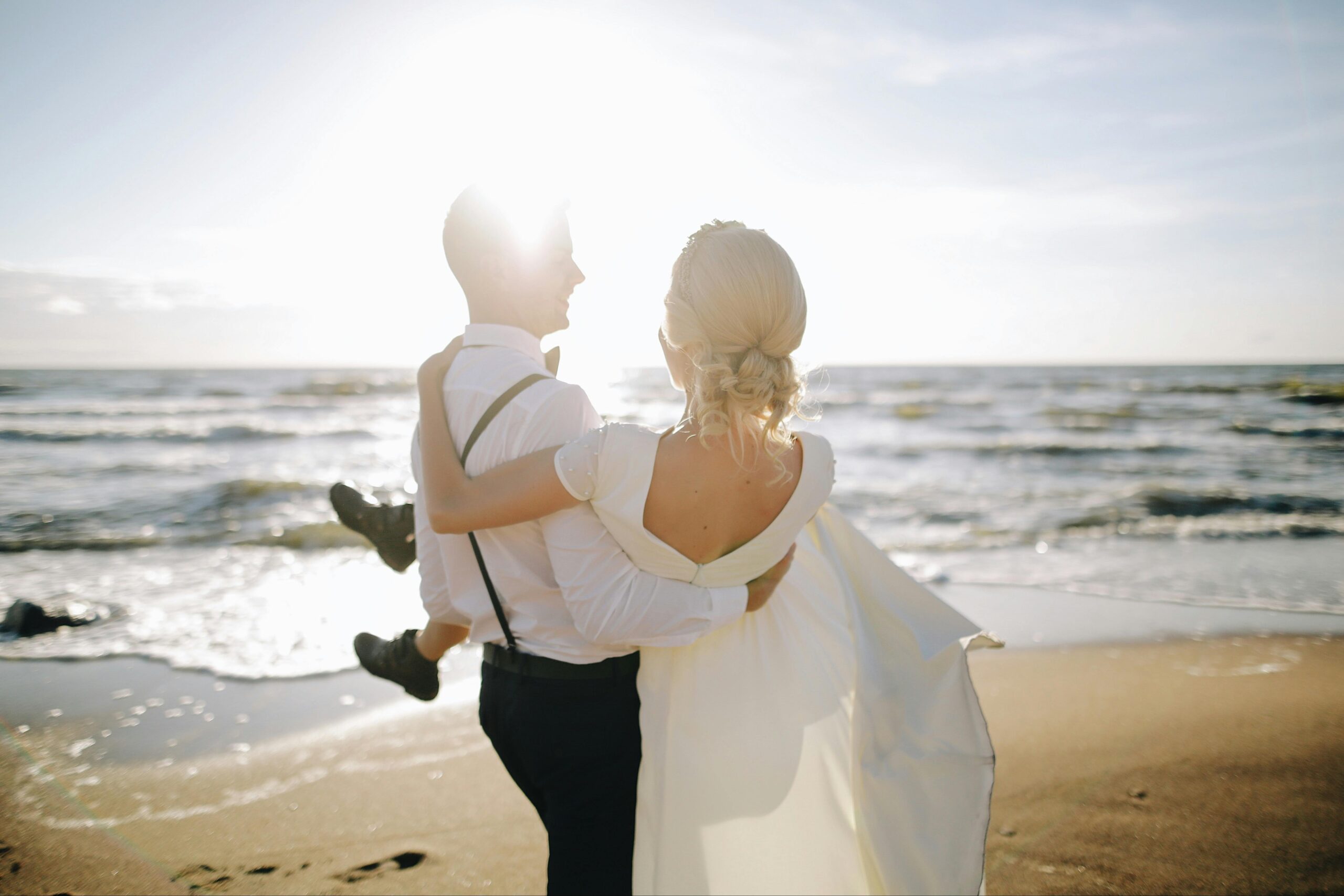 A groom carrying his bride on a sun-drenched beach during their romantic Seychelles honeymoon adventure.