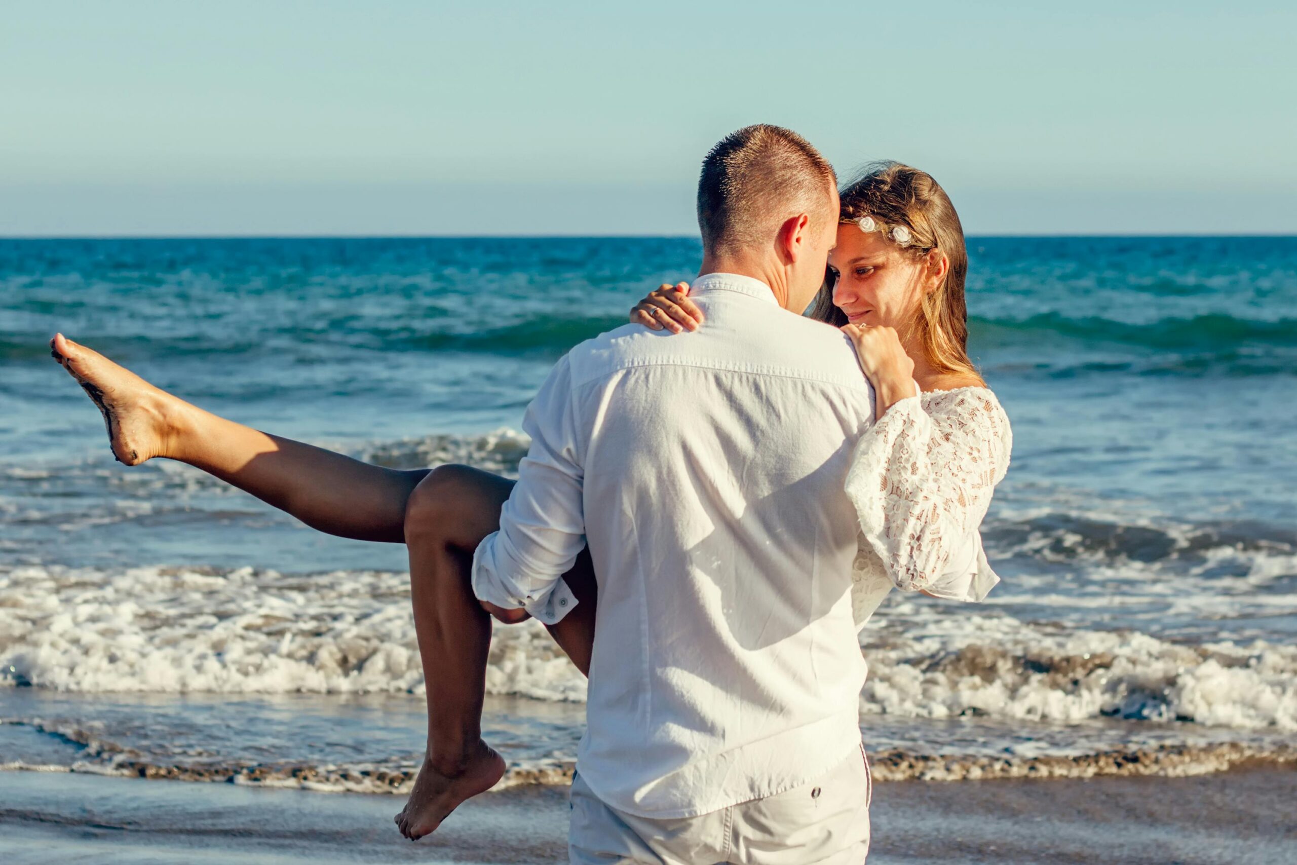 Romantic couple on a tropical beach during a Thailand honeymoon, with the man carrying the woman against the ocean waves.