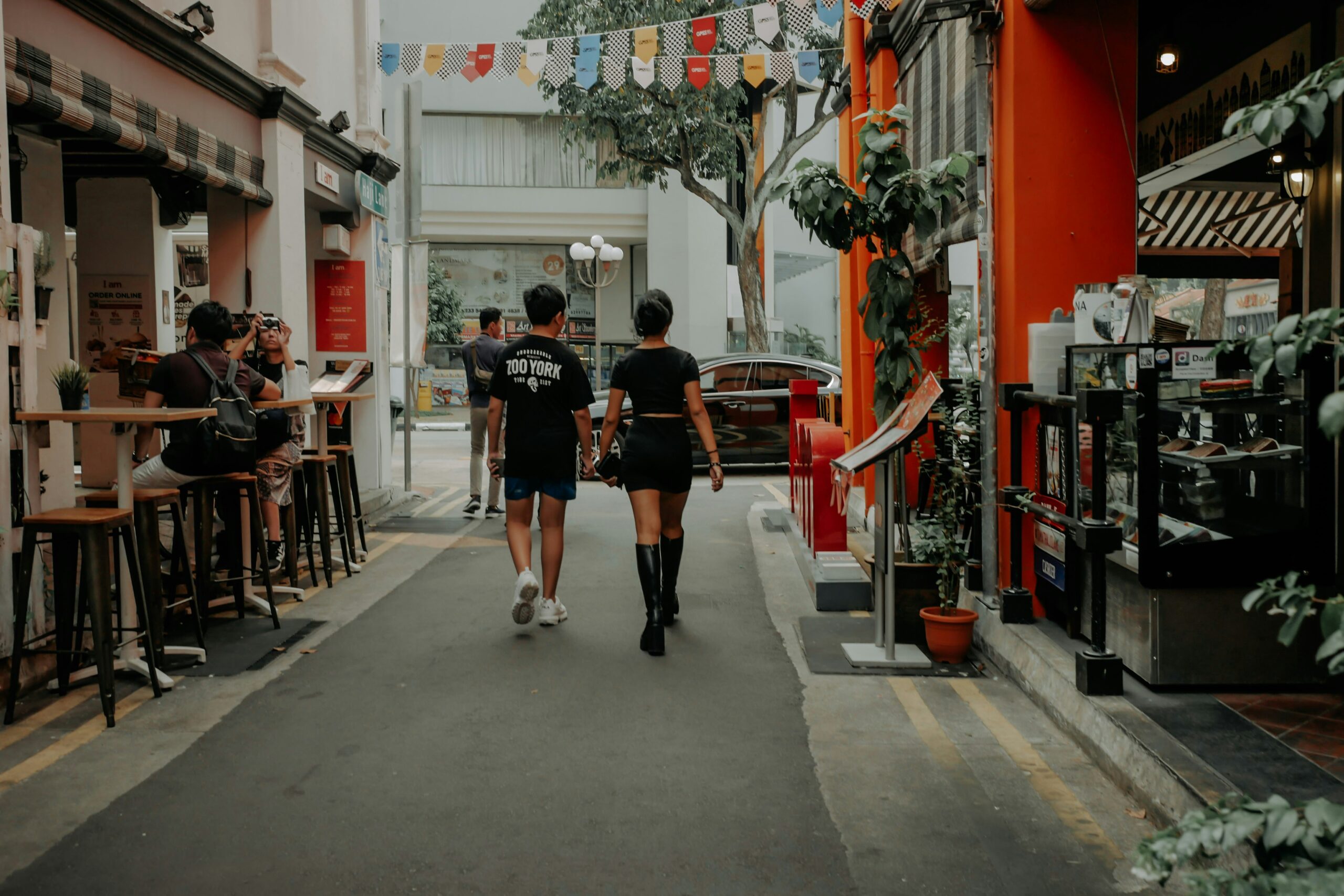 A couple holding hands while walking down a vibrant, café-lined alleyway in Haji Lane, representing fun and energetic date ideas singapore for couples to explore.