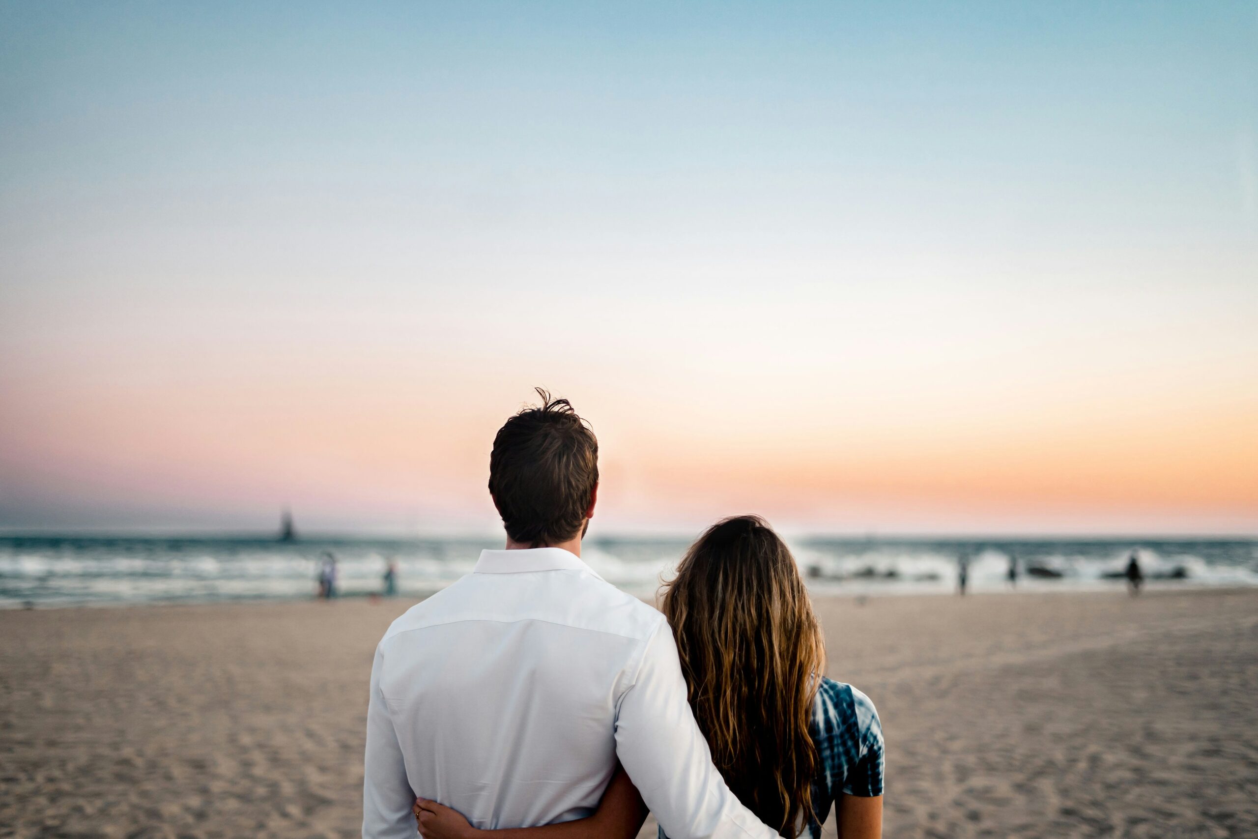 Romantic couple embracing while looking at a beautiful pastel sunset over the ocean on their Thailand honeymoon trip