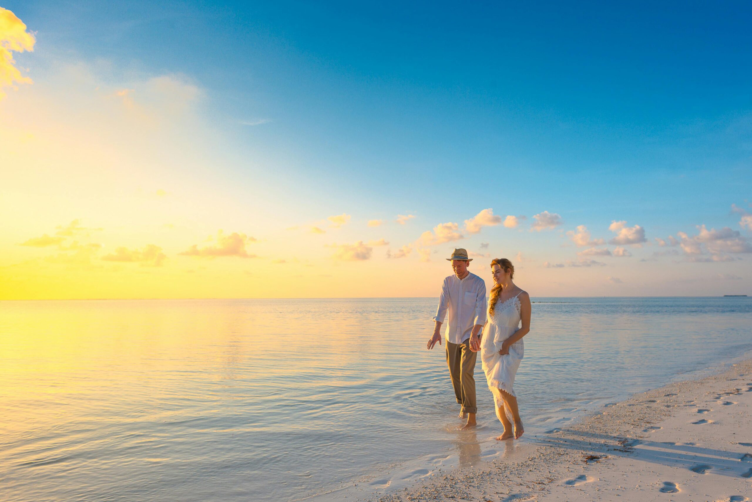 Happy couple walking hand-in-hand on a white sand beach at sunset, enjoying luxury maldives honeymoon travel packages