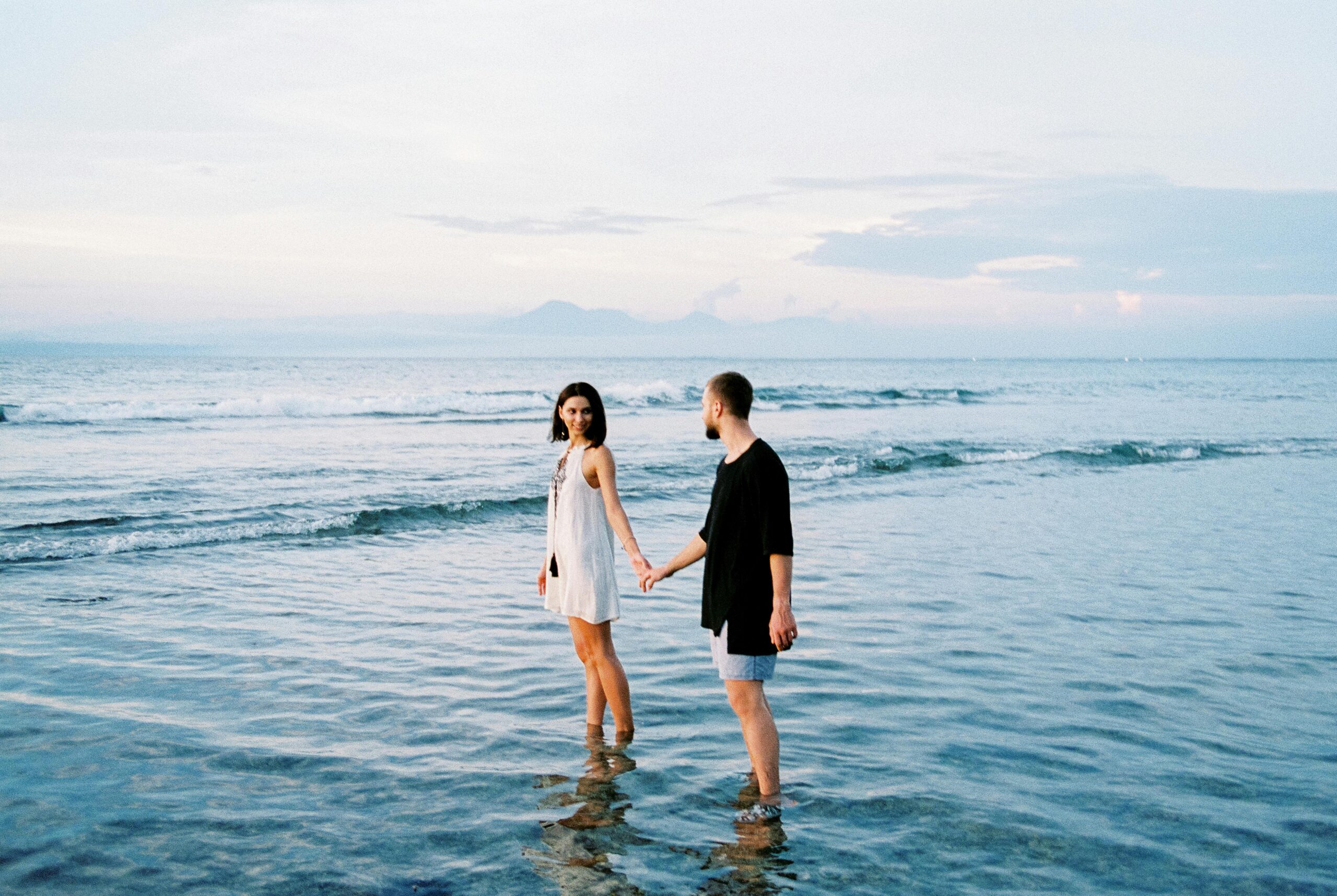 A romantic couple holding hands and smiling in the clear ocean water, showcasing the breathtaking beauty of the best area to stay in bali for couples.