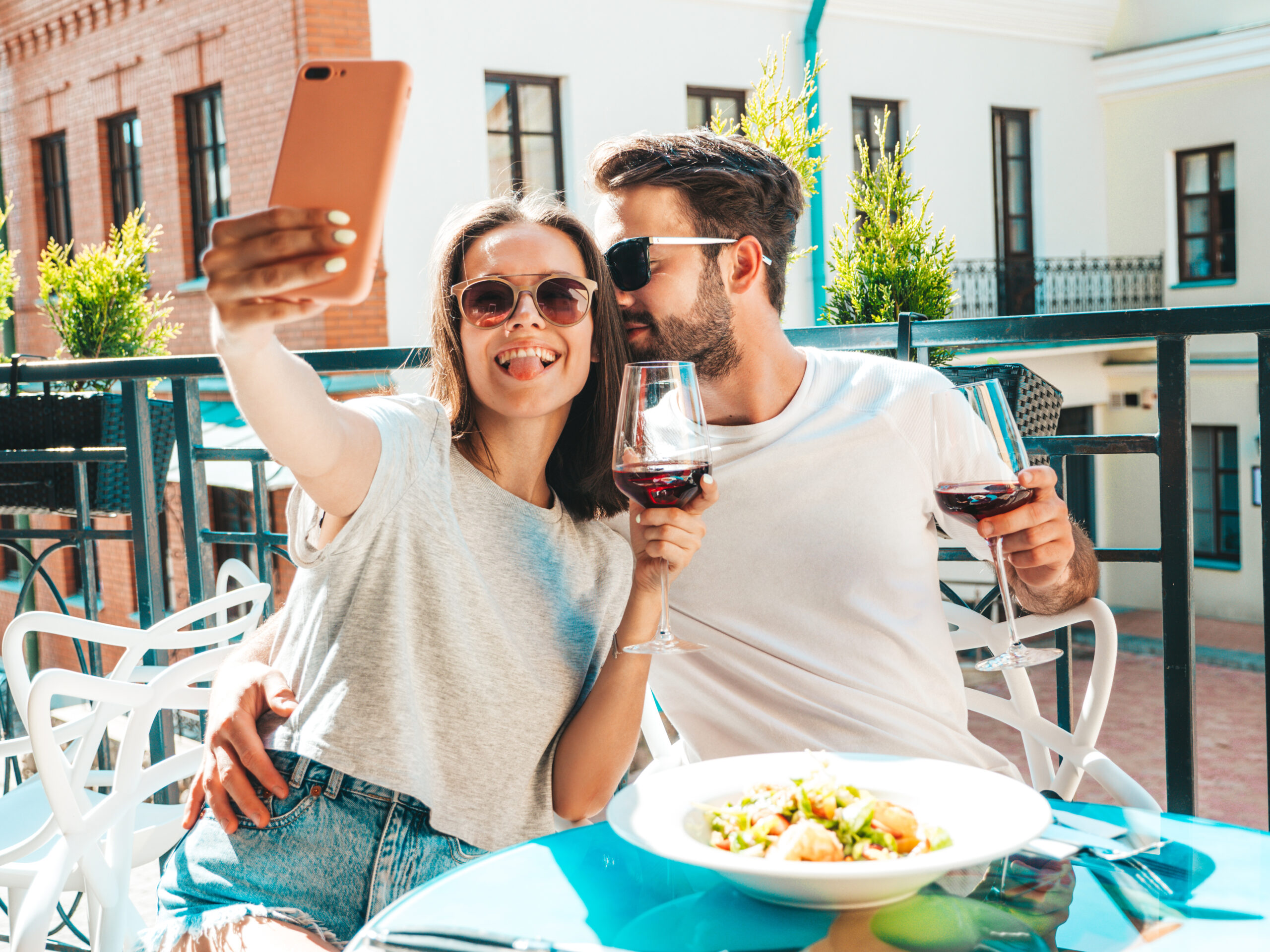 A cheerful couple taking a selfie with red wine at a cozy outdoor restaurant near Secret Hotels in Paris Locals Love